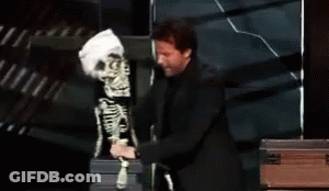 A Man Is Touching A Skeleton Puppet With The Word Touching Behind Him GIF