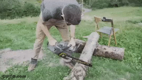 A Man Is Using A Chainsaw To Cut A Log . GIF