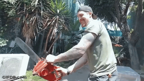 A Man Is Using A Chainsaw To Cut A Tree In A Yard . GIF