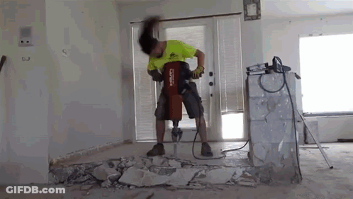 A Man Is Using A Hammer To Break A Wall In A Living Room . GIF