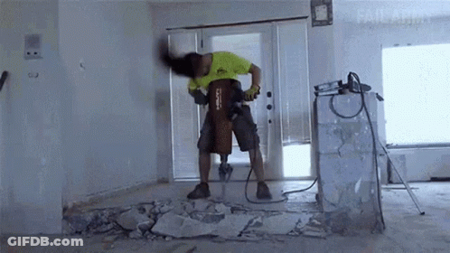 A Man Is Using A Hilti Hammer To Break A Wall GIF