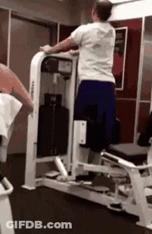 A Man Is Using A Machine In A Gym To Do Squats . GIF