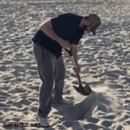 A Man Is Using A Shovel To Dig In The Sand GIF