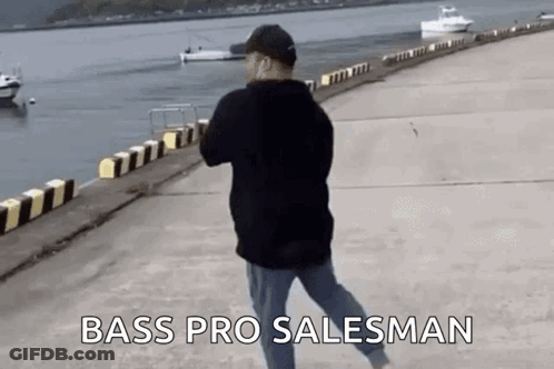 A Man Is Walking Along A Pier Next To A Body Of Water With Boats In The Background . GIF