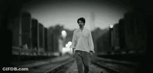 A Man Is Walking Along Train Tracks In A Black And White Photo . GIF