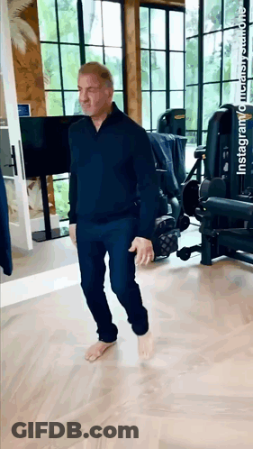 A Man Is Walking Barefoot In A Gym With A Tv On The Wall . GIF