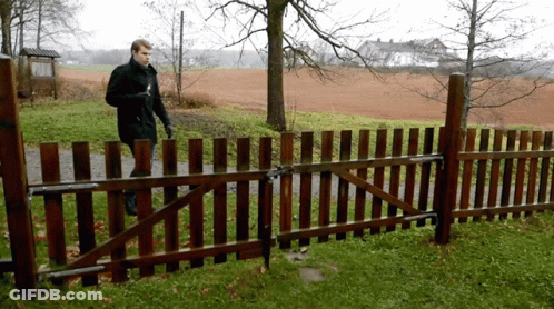 A Man Is Walking Behind A Wooden Fence In A Field GIF