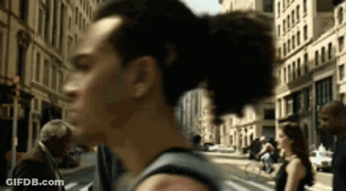 A Man Is Walking Down A City Street With A Woman In The Background . GIF