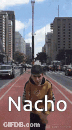 A Man Is Walking Down A City Street With The Word Nacho Written On The Side Of Him . GIF