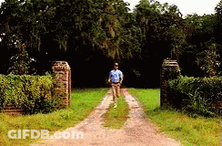 A Man Is Walking Down A Dirt Road In A Field GIF