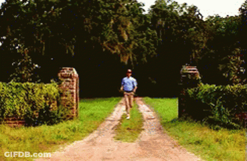 A Man Is Walking Down A Dirt Road In A Field GIF