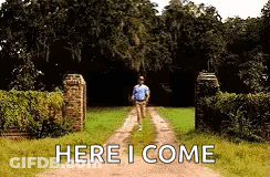 A Man Is Walking Down A Dirt Road With The Words `` Here I Come '' Written On The Ground . GIF