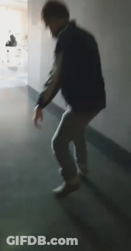 A Man Is Walking Down A Hallway In A Dark Room . GIF