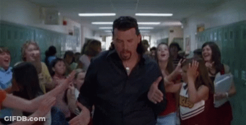 A Man Is Walking Down A Hallway Surrounded By Cheerleaders . GIF