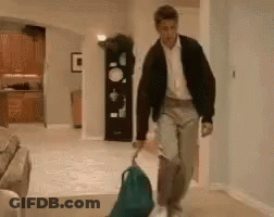 A Man Is Walking Down A Hallway With A Backpack And A Suitcase . GIF