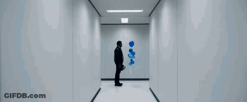 A Man Is Walking Down A Hallway With A Blue Bottle In His Hand . GIF
