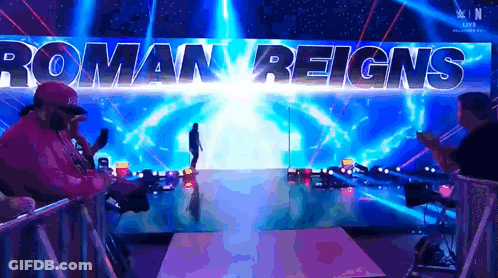 A Man Is Walking Down A Ramp With Roman Reigns Written On The Wall Behind Him GIF