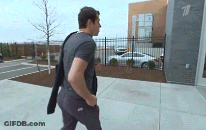 A Man Is Walking Down A Sidewalk In Front Of A Building With A Car Parked In Front Of It . GIF