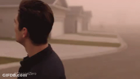 A Man Is Walking Down A Street In Front Of A House In The Fog . GIF