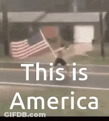 A Man Is Walking Down The Street With An American Flag In The Background . GIF