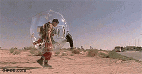 A Man Is Walking In A Clear Bubble On The Side Of A Road . GIF