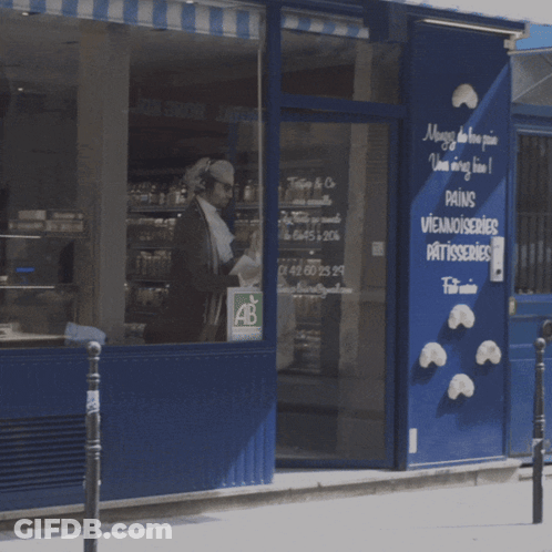 A Man Is Walking In Front Of A Store That Sells Pains Viennoiseries Patisseries GIF