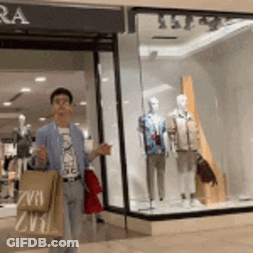 A Man Is Walking In Front Of A Store With A Bag That Says Zvra GIF