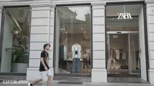 A Man Is Walking In Front Of A Store With A Mannequin In The Window . GIF