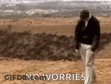 A Man Is Walking On A Dirt Road With The Words `` No Worries '' Written On The Ground . GIF