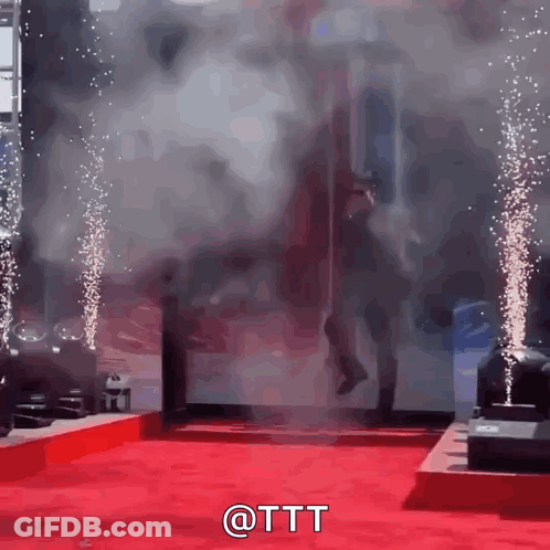 A Man Is Walking On A Red Carpet With Smoke Coming Out Of The Door GIF