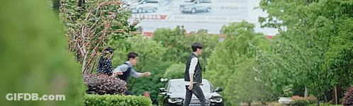 A Man Is Walking Past A Car In A Park . GIF