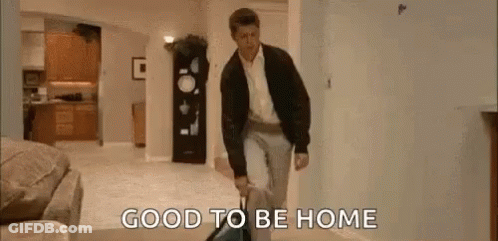 A Man Is Walking Through A Living Room Carrying A Suitcase And A Vacuum Cleaner . GIF
