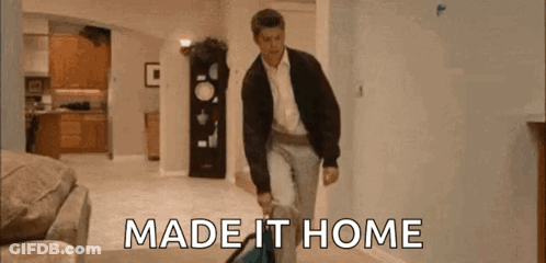 A Man Is Walking Through A Living Room Carrying A Suitcase And The Words `` Made It Home '' . GIF