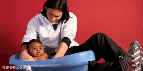 A Man Is Washing A Baby In A Blue Bathtub GIF