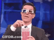 A Man Is Wearing 3D Glasses And Holding A Popcorn Box GIF