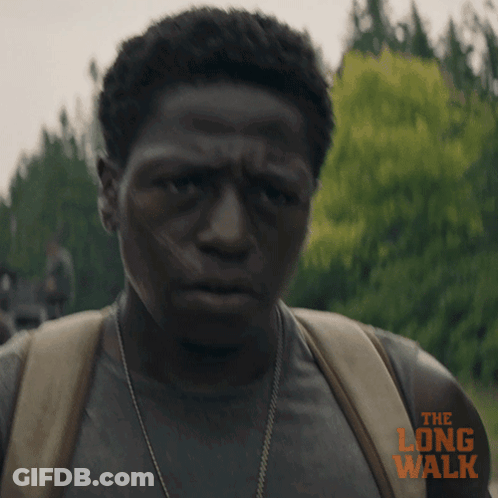 A Man Is Wearing A Backpack And A Shirt That Says The Long Walk On It GIF