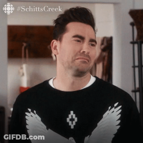 A Man Is Wearing A Black Sweater With White Wings On The Front GIF