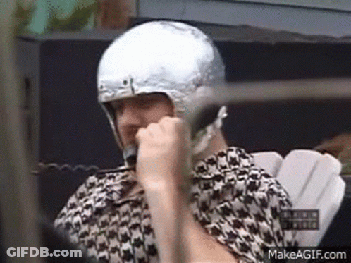 A Man Is Wearing A Silver Helmet And Talking On A Cell Phone . GIF