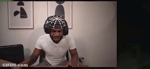 A Man Is Wearing A Spider Web Hat And Headphones While Sitting At A Desk . GIF