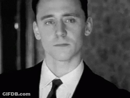 A Man Is Wearing A Suit And Tie And Looking At The Camera . GIF