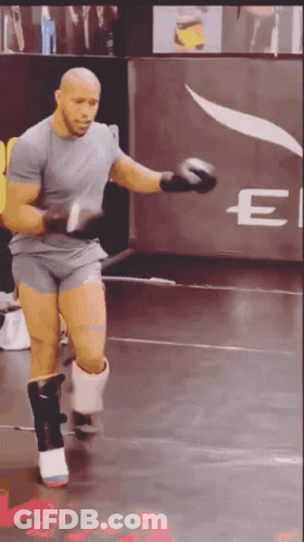 A Man Is Wearing Boxing Gloves In Front Of A Sign That Says E GIF