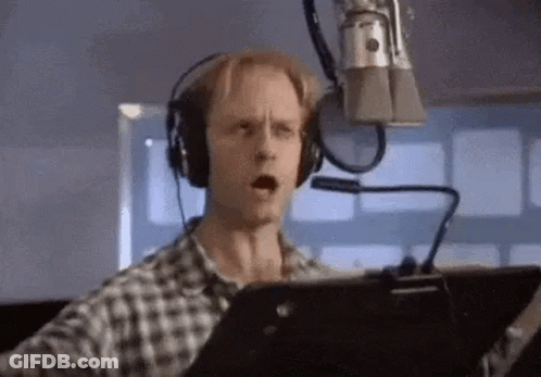 A Man Is Wearing Headphones And Singing Into A Microphone . GIF