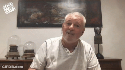 A Man Is Wearing Headphones In Front Of A Painting That Says " Good Bad Rugby " GIF