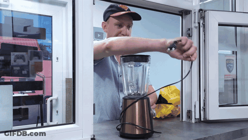 A Man Is Working On A Blender In Front Of A Window That Has A Sticker That Says ' Safety ' GIF