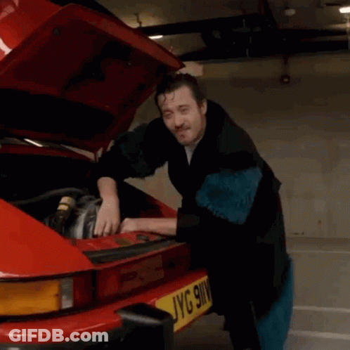 A Man Is Working On A Red Car With The Hood Up And A License Plate That Says Jyg 9Wv GIF