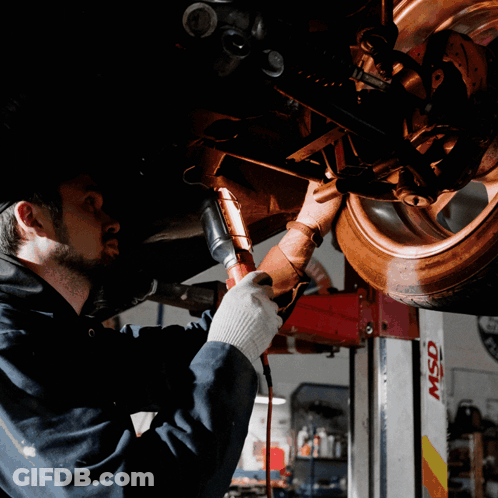 A Man Is Working Under A Car In A Garage With A Msd Lift In The Background GIF