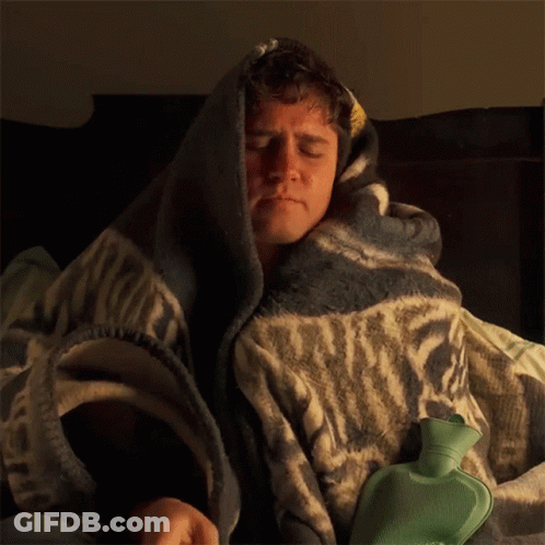 A Man Is Wrapped In A Blanket With A Green Hot Water Bottle GIF