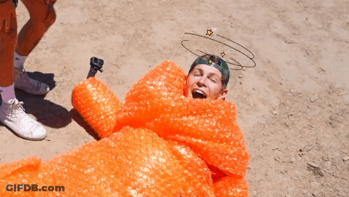 A Man Is Wrapped In Orange Bubble Wrap With A Drawing Of Stars On His Head GIF