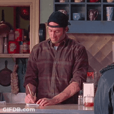 A Man Is Writing On A Notepad In Front Of A Shelf With Ketchup GIF