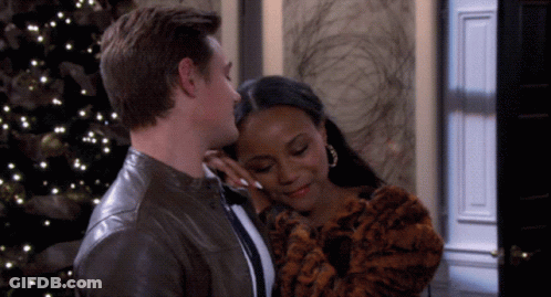 A Man Kisses A Woman On The Forehead In Front Of A Christmas Tree GIF